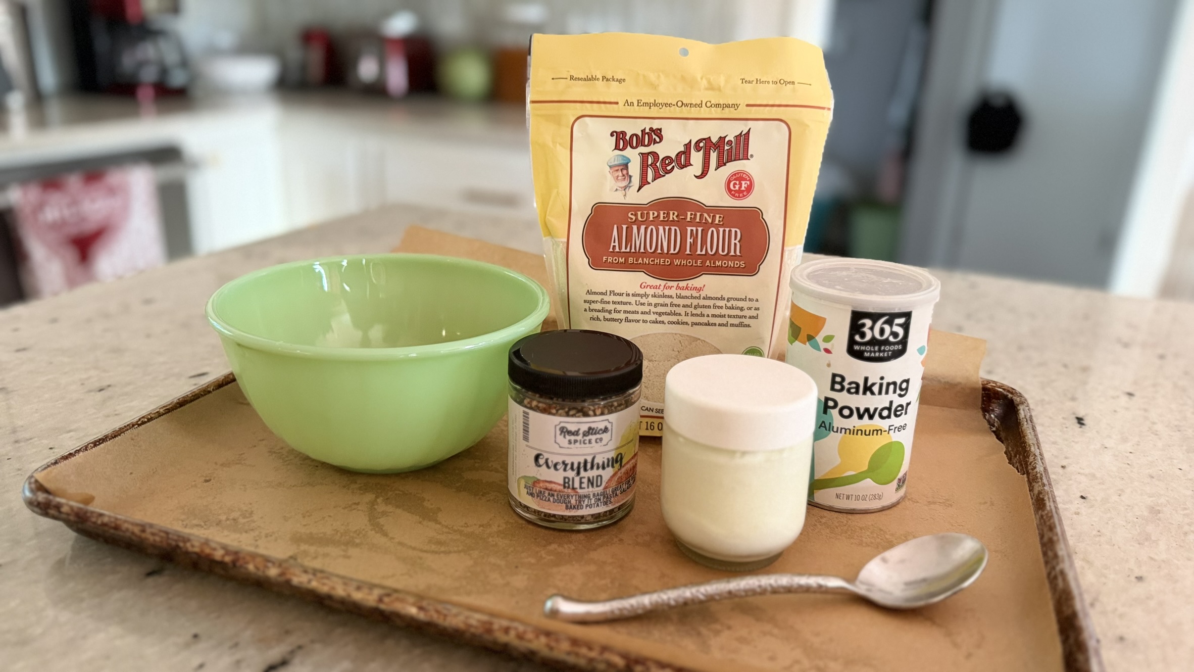Ingredients for bagel bites on a baking sheet: almond flour, yogurt, baking powder and everything bagel seasoning